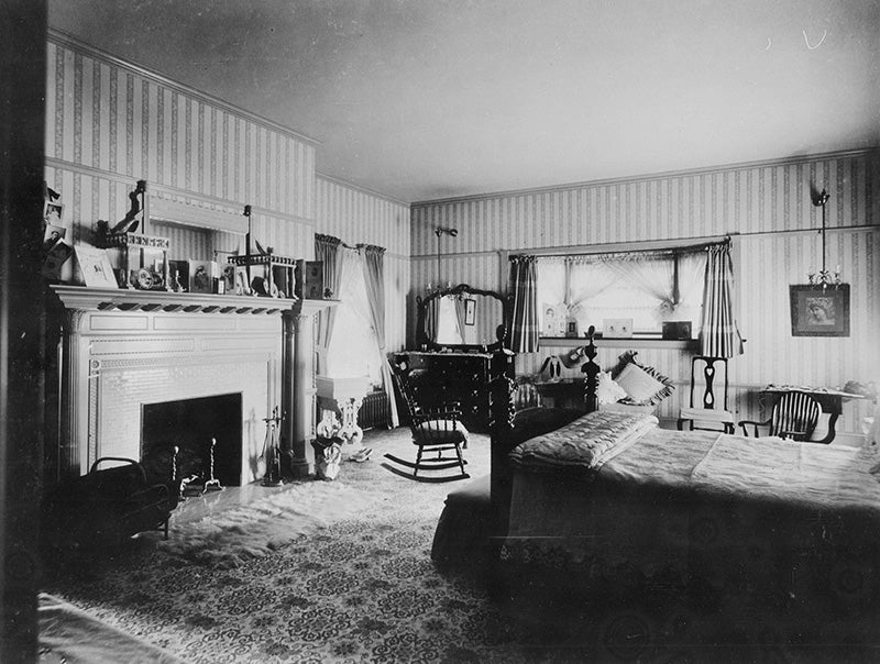 A bedroom in the Hord residence with a colonial style fireplace, wallpaper, wall to wall rug, and gas light fixtures. Click on the image to explore the collection.